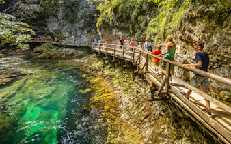 Visitors walking on the boardwalk at Vintgar Gorge, Slovenia, with clear water below.