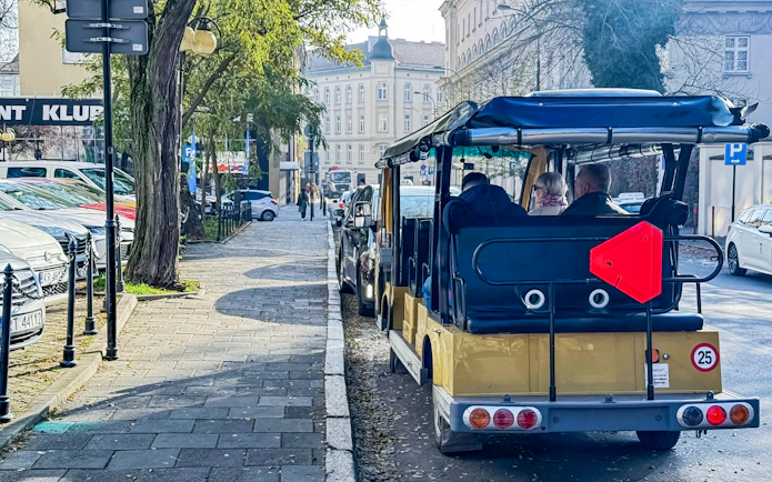 Golf cart tour in Krakow Old Town along a tree-lined street.