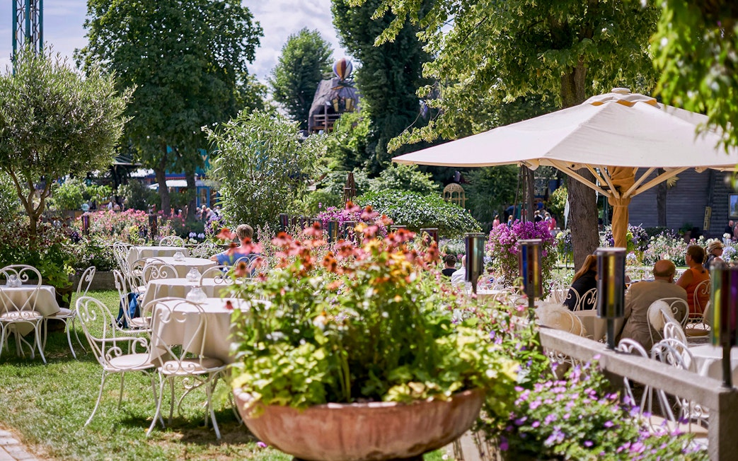 Outdoor dining area with tables and chairs surrounded by flowers at Tivoli Gardens.