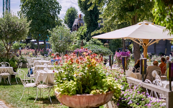 Outdoor dining area with tables and chairs surrounded by flowers at Tivoli Gardens.