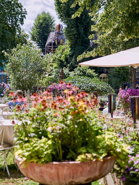 Outdoor dining area with tables and chairs surrounded by flowers at Tivoli Gardens.
