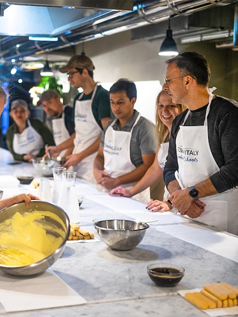 Participants in a Florence pasta-making class whisking ingredients at a kitchen counter.