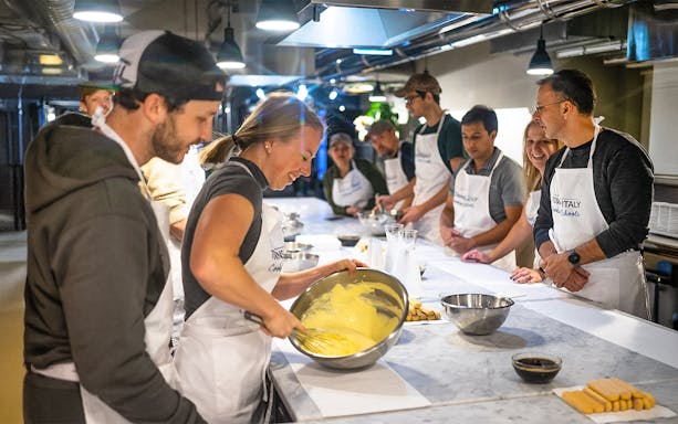 Participants in a Florence pasta-making class whisking ingredients at a kitchen counter.