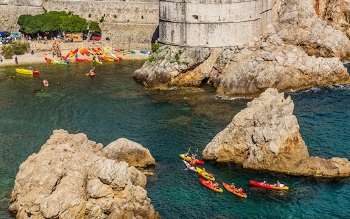 Kayakers paddling near Dubrovnik's historic city walls and rocky coastline.