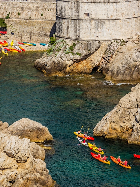 Kayakers paddling near Dubrovnik's historic city walls and rocky coastline.
