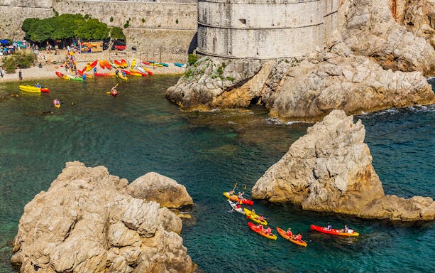 Kayakers paddling near Dubrovnik's historic city walls and rocky coastline.