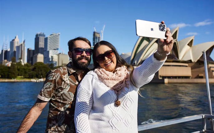 Couple taking a selfie on a Sydney Harbour Cruise with the Opera House in the background.