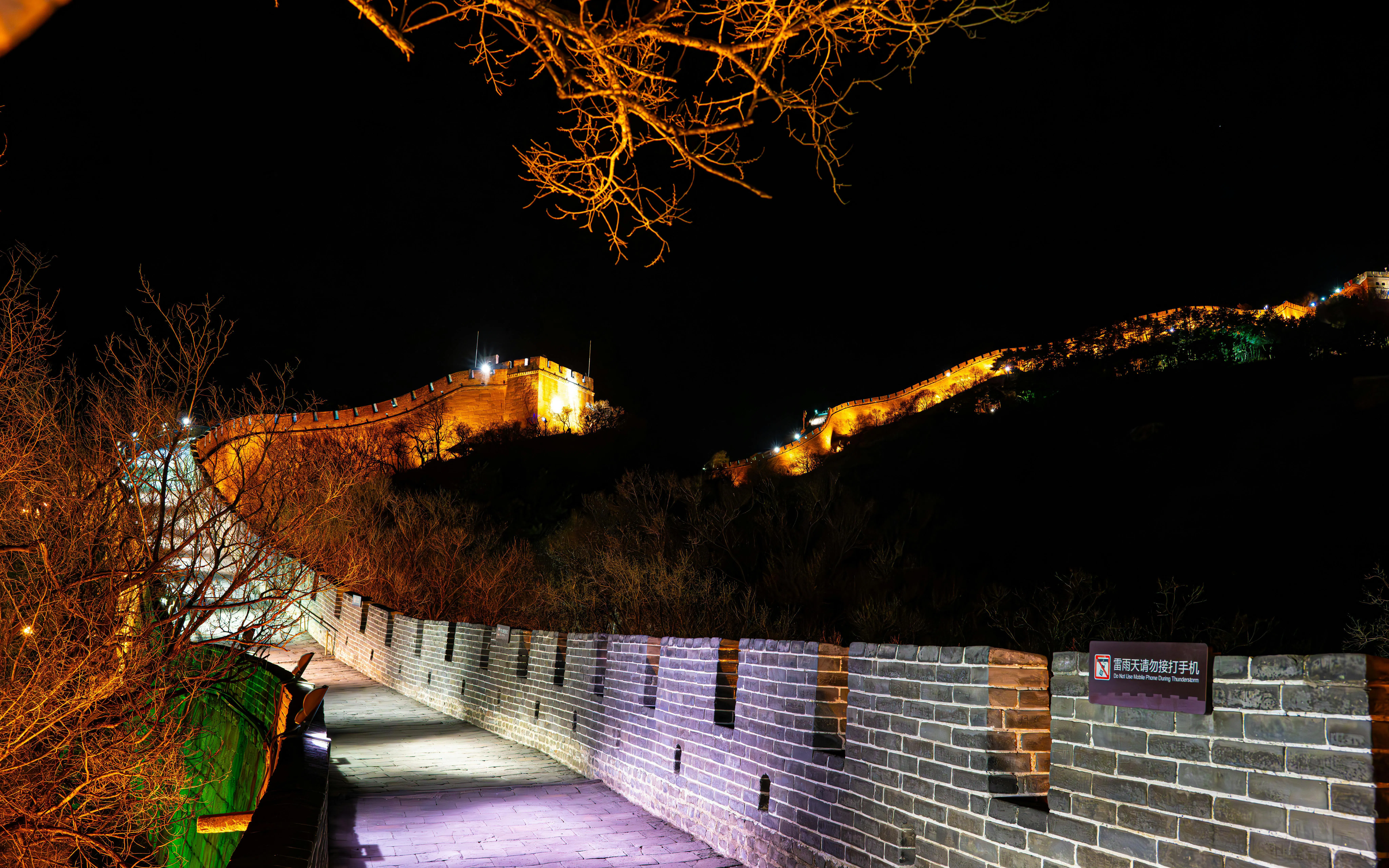 Badaling Great Wall illuminated at night, Beijing, with lit pathway and surrounding trees.