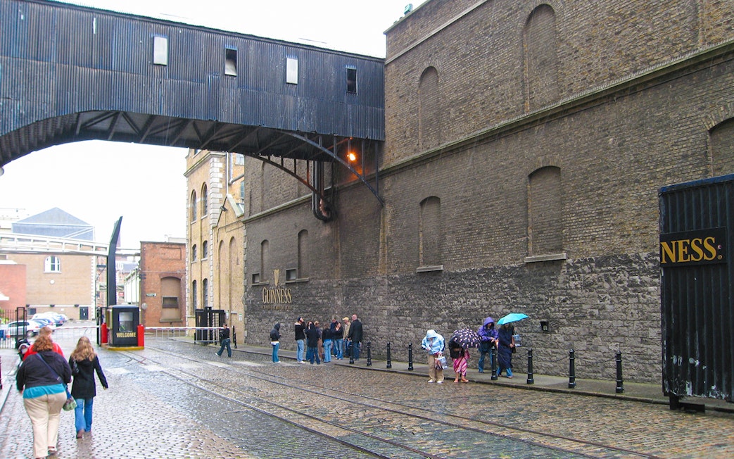 Guinness Storehouse exterior with visitors walking on cobblestone street in Dublin.