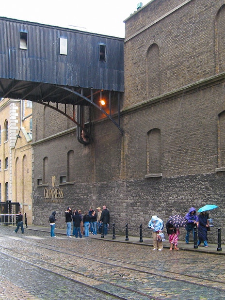 Guinness Storehouse exterior with visitors walking on cobblestone street in Dublin.