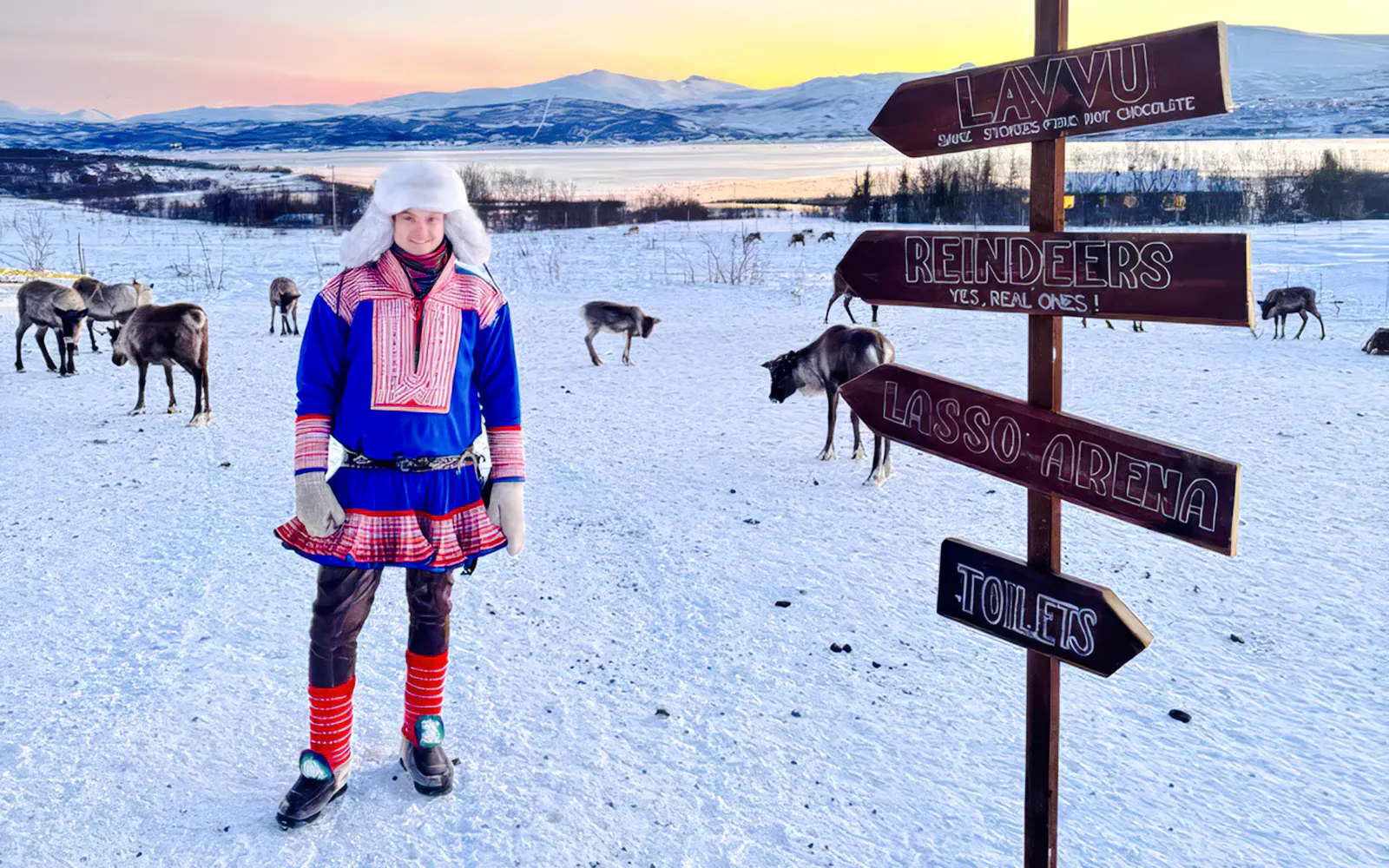 Sami person in traditional attire with reindeer in snowy Tromsø landscape.