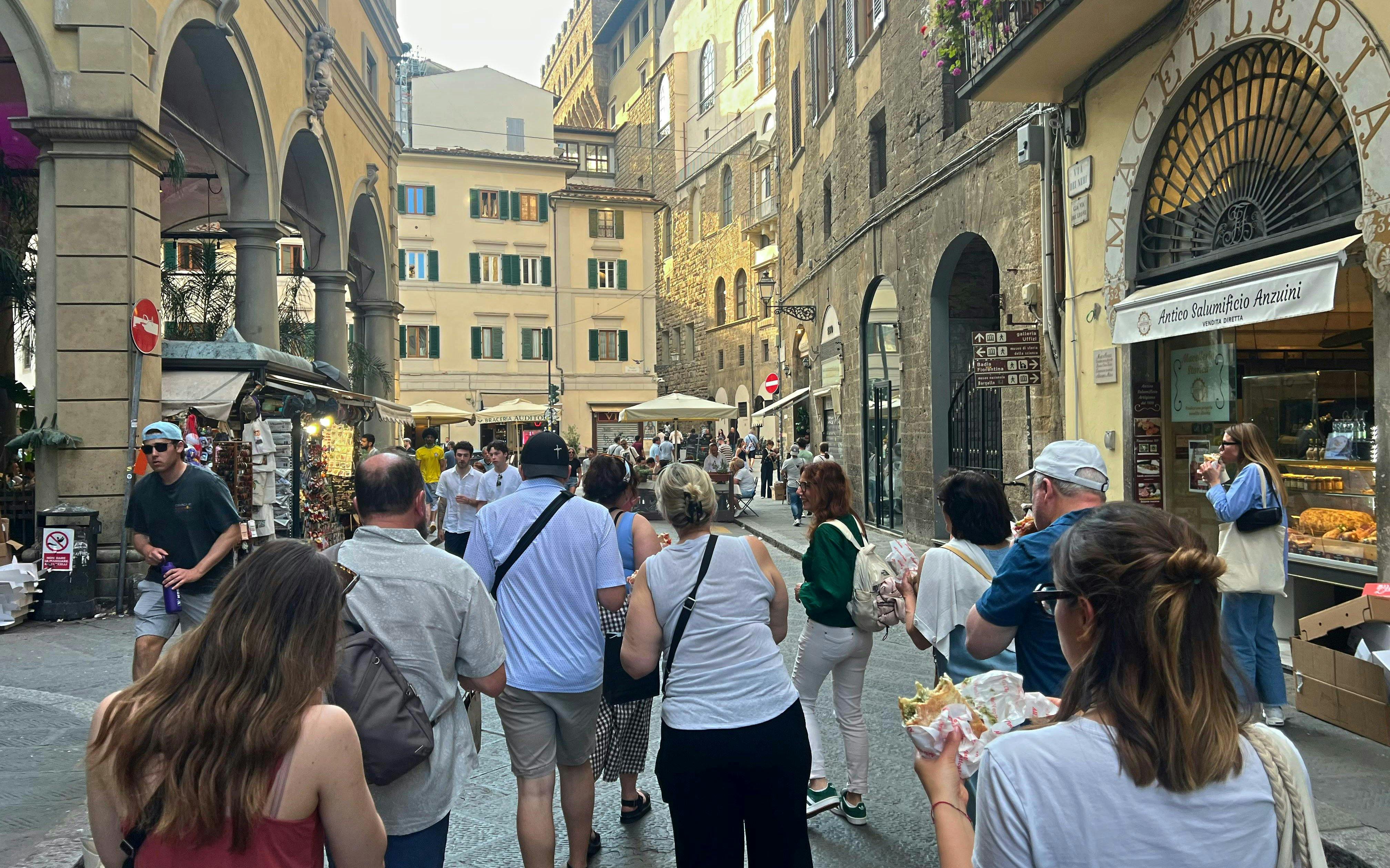 Tourists exploring a street in Florence, Italy, enjoying local food near historic buildings.