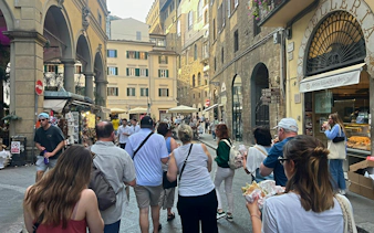 Tourists exploring a street in Florence, Italy, enjoying local food near historic buildings.