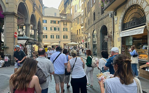 Tourists exploring a street in Florence, Italy, enjoying local food near historic buildings.
