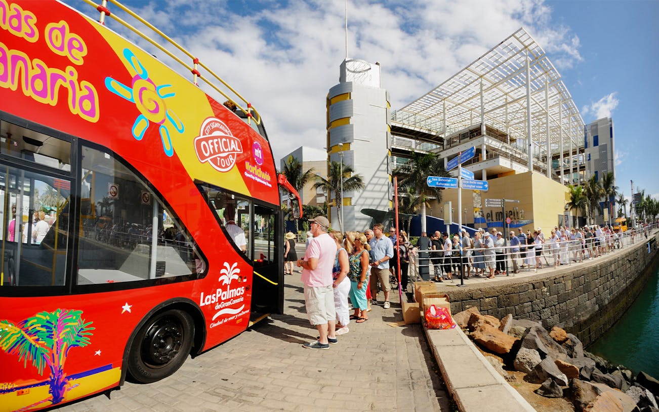 Hop-On Hop-Off bus with tourists boarding in Las Palmas de Gran Canaria near waterfront.