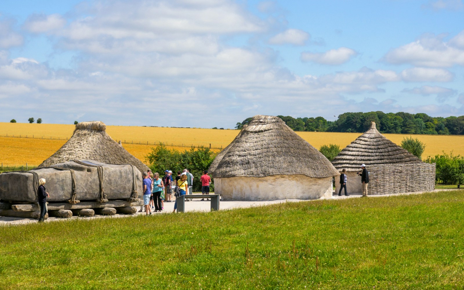 Reconstructed Neolithic houses near Stonehenge with visitors exploring the site.
