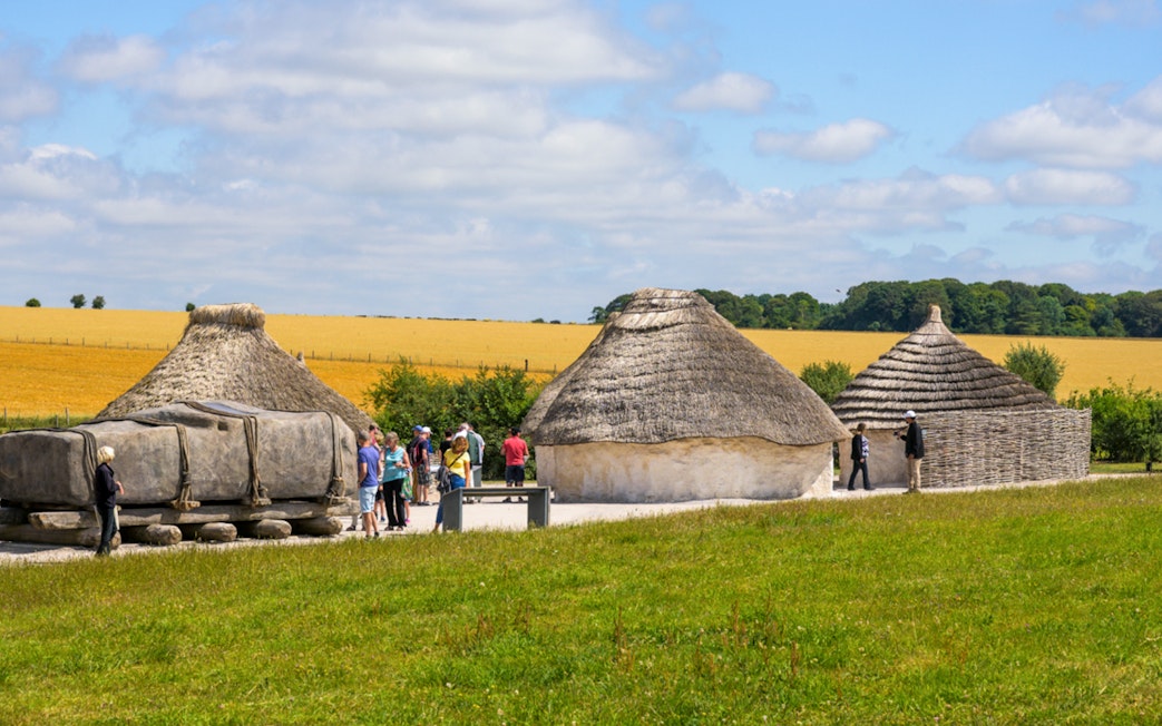 Reconstructed Neolithic houses near Stonehenge with visitors exploring the site.