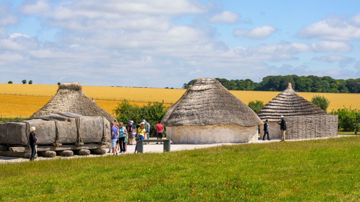 Reconstructed Neolithic houses near Stonehenge with visitors exploring the site.