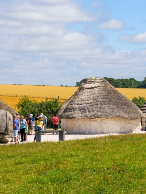 Reconstructed Neolithic houses near Stonehenge with visitors exploring the site.