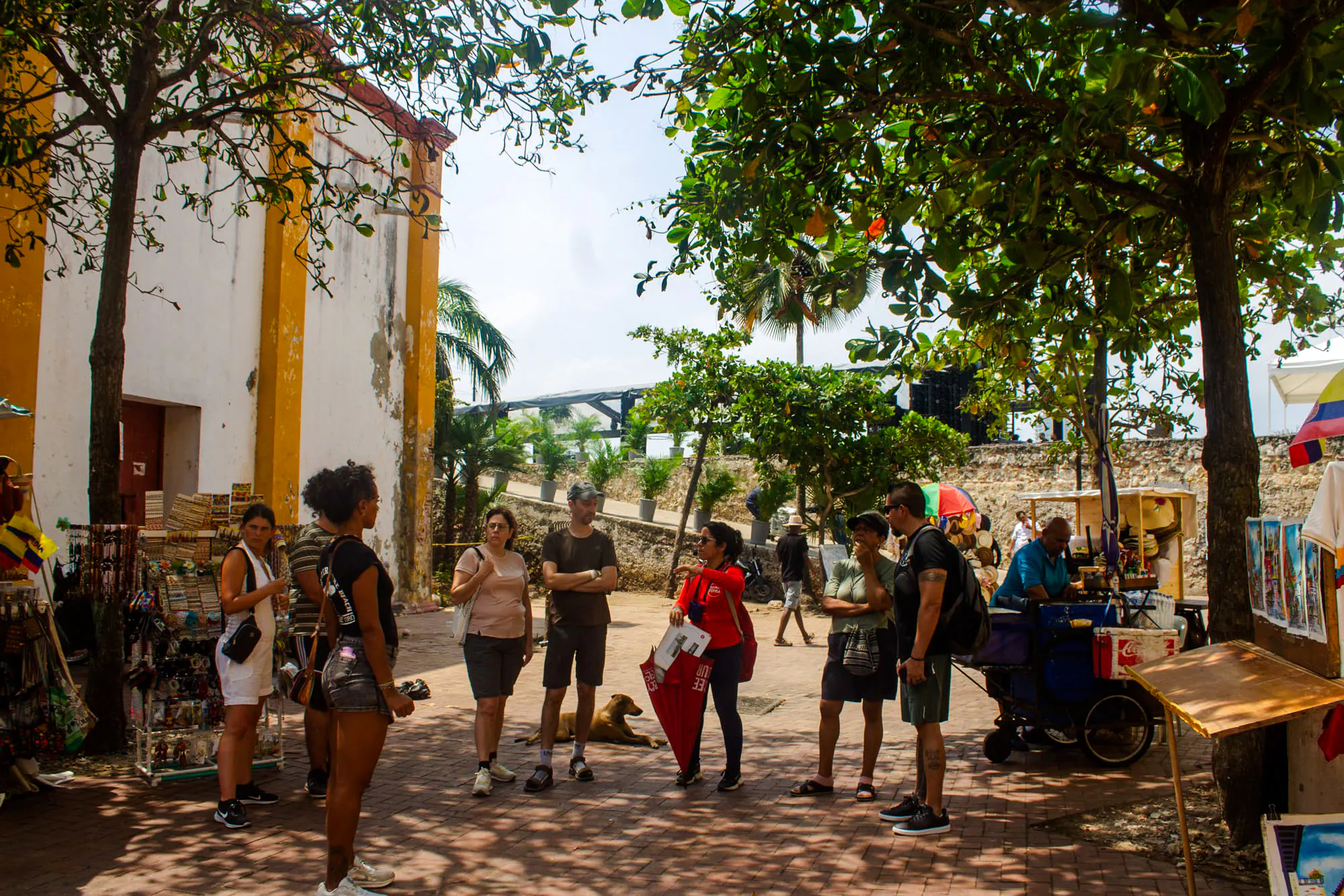 Tour group exploring Cartagena's Walled Old City with guide, near local vendors and historic architecture.