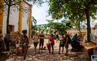 Tour group exploring Cartagena's Walled Old City with guide, near local vendors and historic architecture.