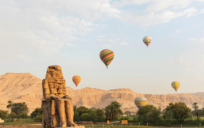 Hot air balloons over Colossi of Memnon in Luxor at sunrise.