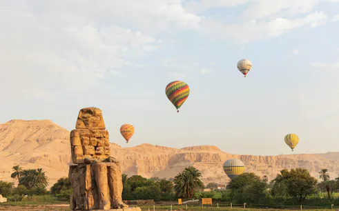 Hot air balloons over Colossi of Memnon in Luxor at sunrise.