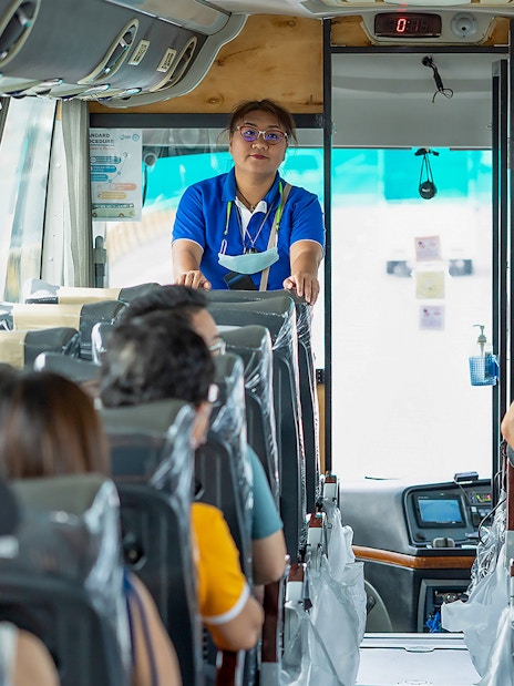 Tour guide speaking to passengers on a bus during Bangkok tour.