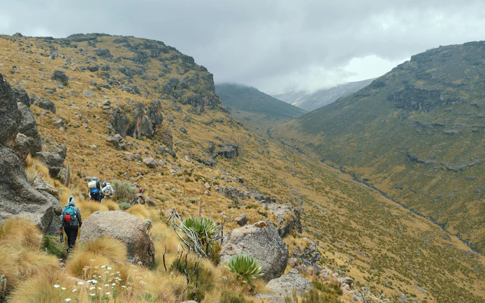 Hikers trekking through Mackinder's Valley, Mount Kenya, surrounded by rocky terrain and vegetation.