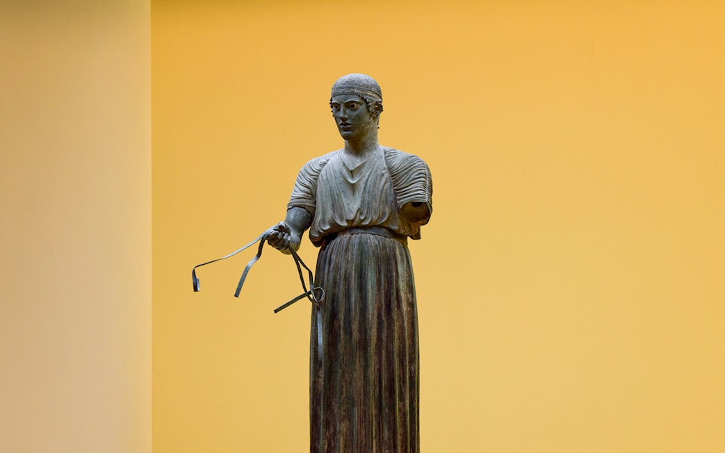 Sculpture of a charioteer holding reins inside Delphi Museum.