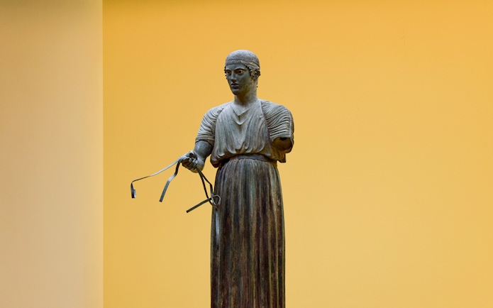 Sculpture of a charioteer holding reins inside Delphi Museum.
