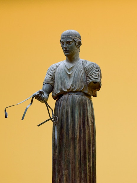 Sculpture of a charioteer holding reins inside Delphi Museum.