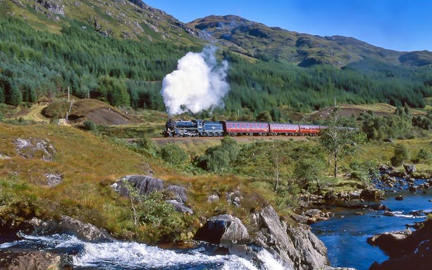 Jacobite Steam Train traveling through the Scottish Highlands with scenic mountain backdrop.