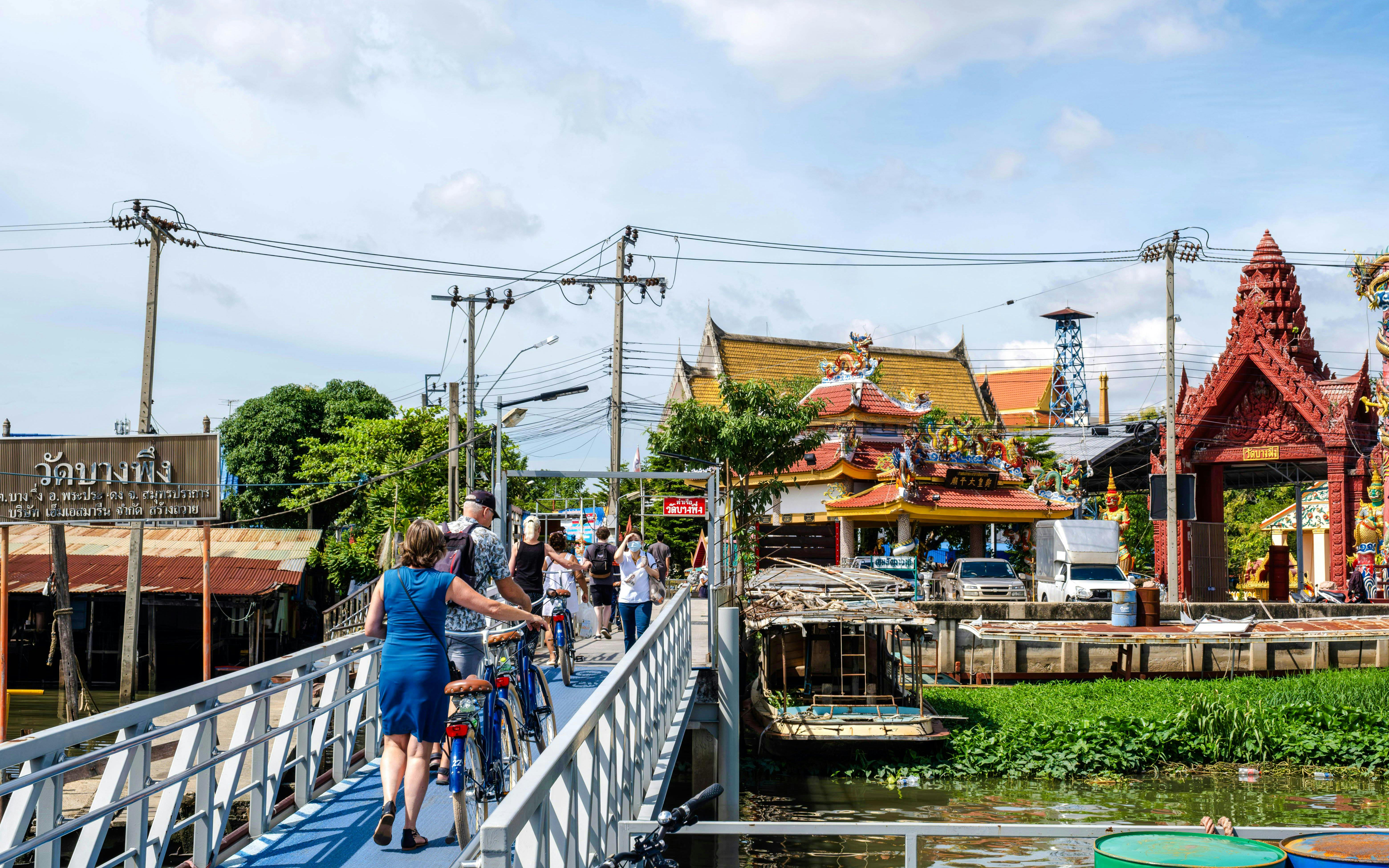 Tourists with bicycles crossing a bridge near a temple in Bangkok, Thailand.
