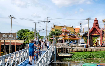 Tourists with bicycles crossing a bridge near a temple in Bangkok, Thailand.