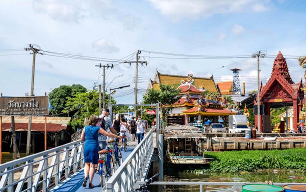 Tourists with bicycles crossing a bridge near a temple in Bangkok, Thailand.