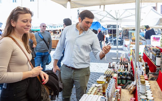 Tourists exploring a market stall with local products in Campo de' Fiori, Rome.
