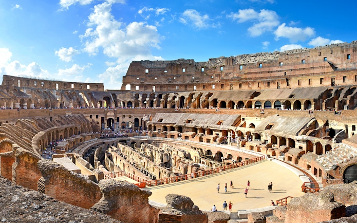 Colosseum Arena interior with tourists exploring ancient Roman architecture in Rome, Italy.