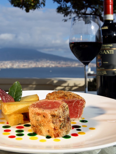 Seared tuna and wine on a rooftop terrace with Mount Vesuvius view in Naples.