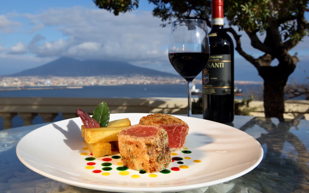 Seared tuna and wine on a rooftop terrace with Mount Vesuvius view in Naples.
