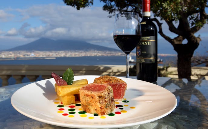 Seared tuna and wine on a rooftop terrace with Mount Vesuvius view in Naples.