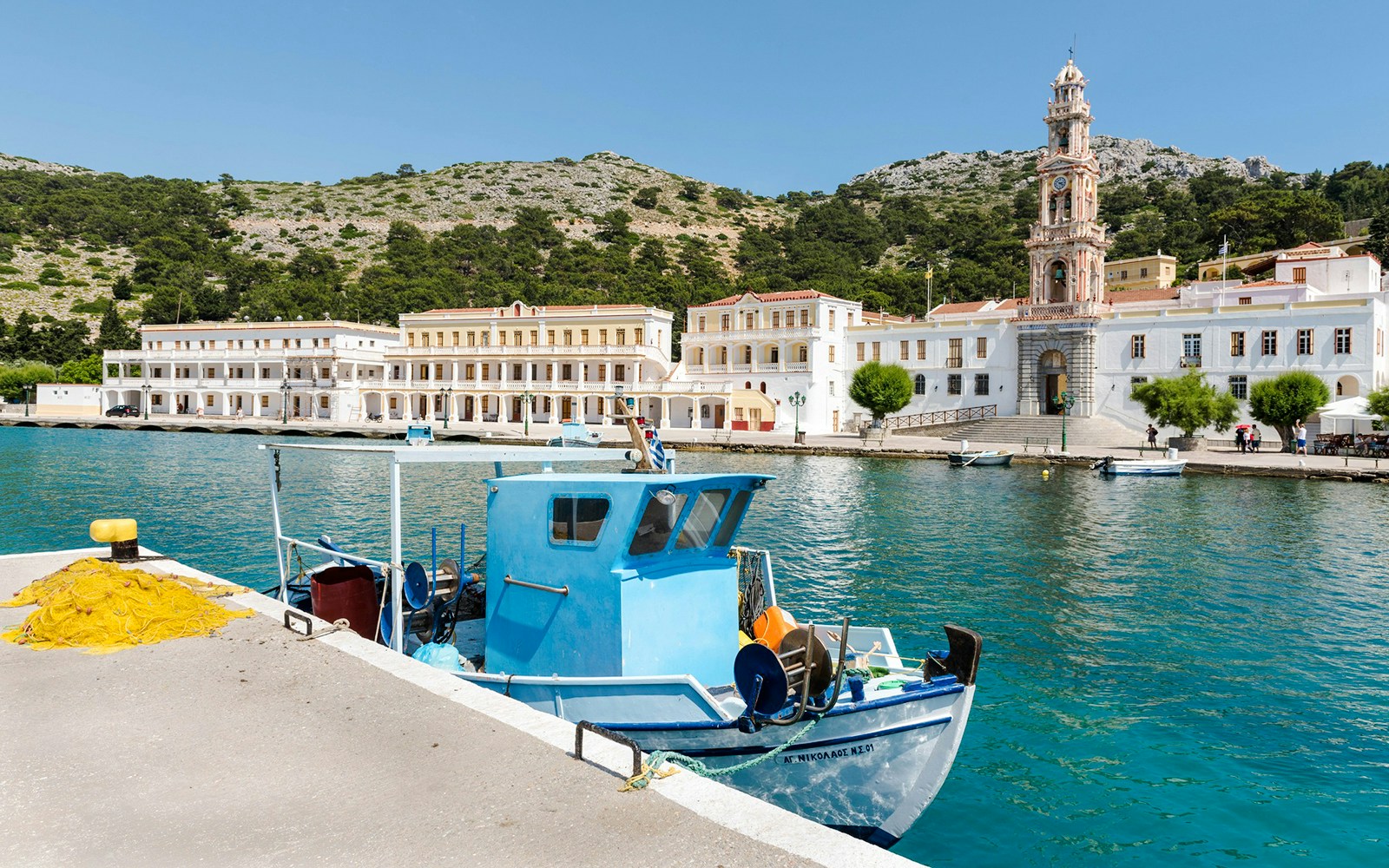 Fishing boat docked at Symi pier with historic buildings and clock tower in the background, Rhodes.