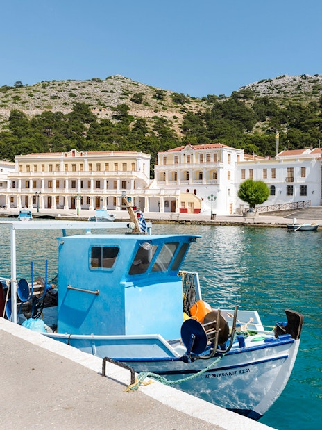 Fishing boat docked at Symi pier with historic buildings and clock tower in the background, Rhodes.