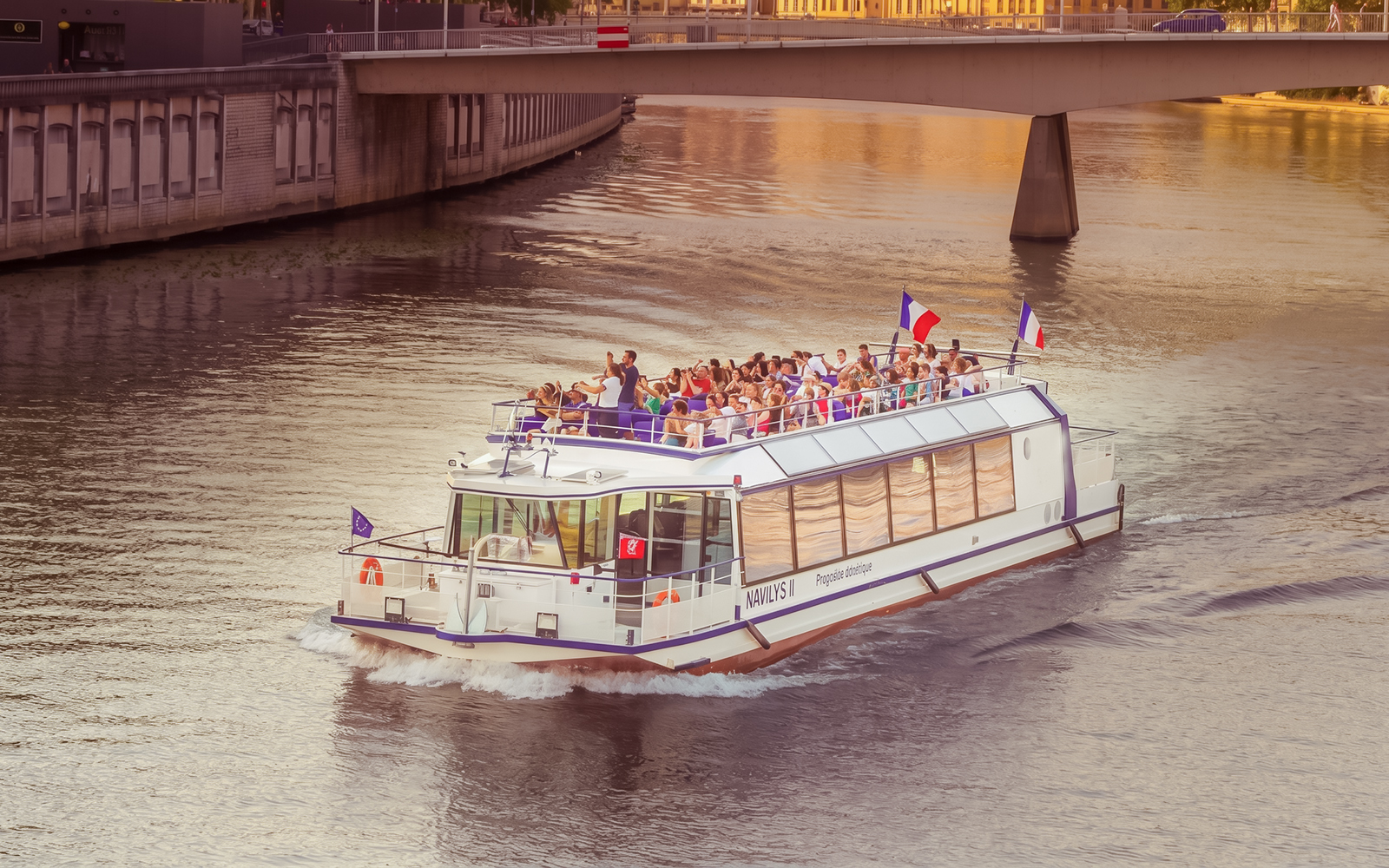 Tour boat cruising on the Saône River in Lyon with passengers enjoying the view.