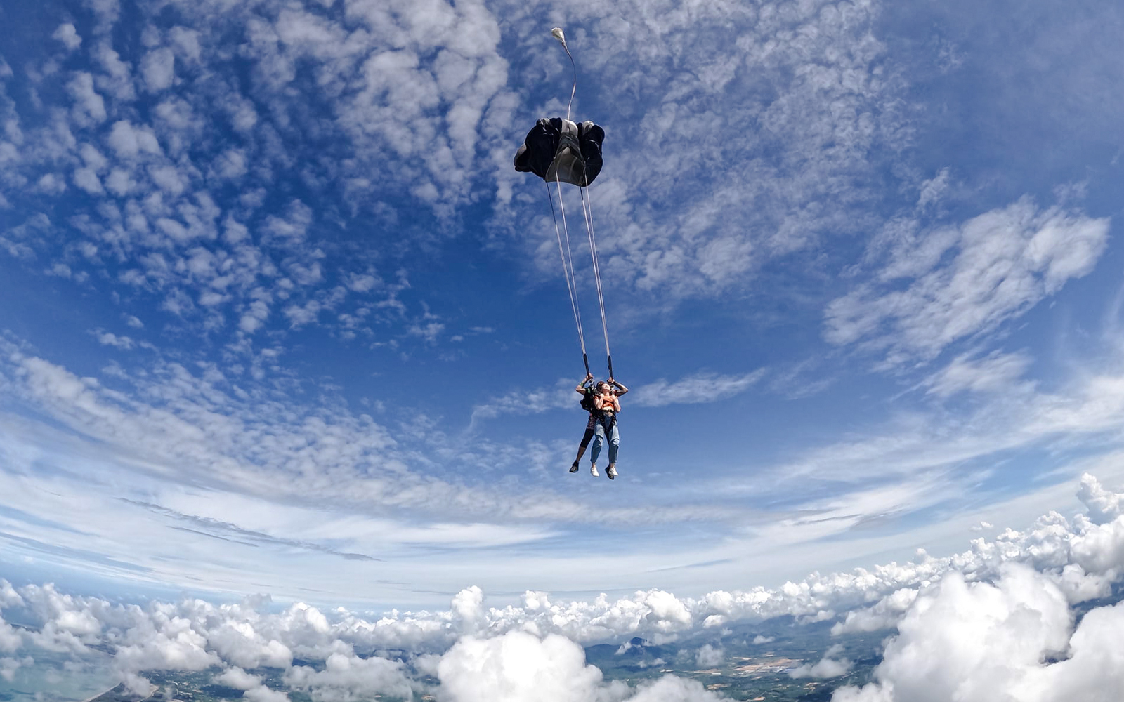 Tourist tandem skydiving with parachute over scenic landscape.