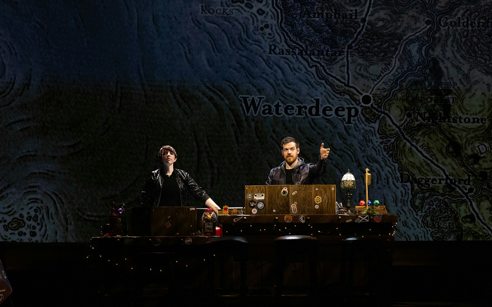 Two people at a table with a map of Waterdeep in the background during Dungeons & Dragons: The Twenty-Sided Tavern.