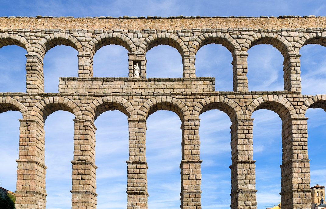 Double-tiered arches of the Aqueduct of Segovia against a blue sky.