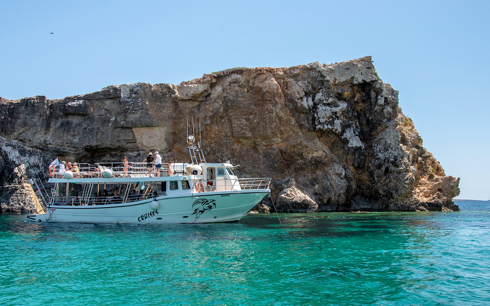 Cruise boat near rocky cliffs at Blue Lagoon, clear turquoise water.