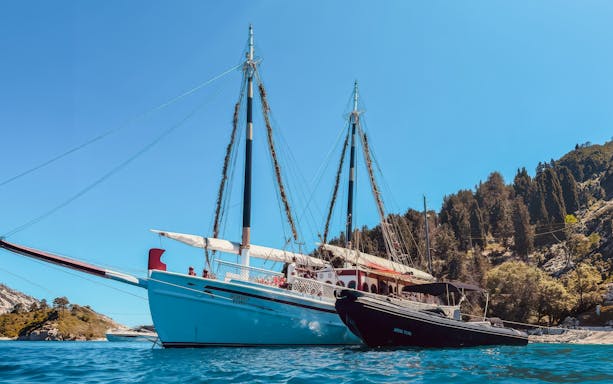Sailing boats anchored near the coast of Corfu, Greece, with lush hills in the background.