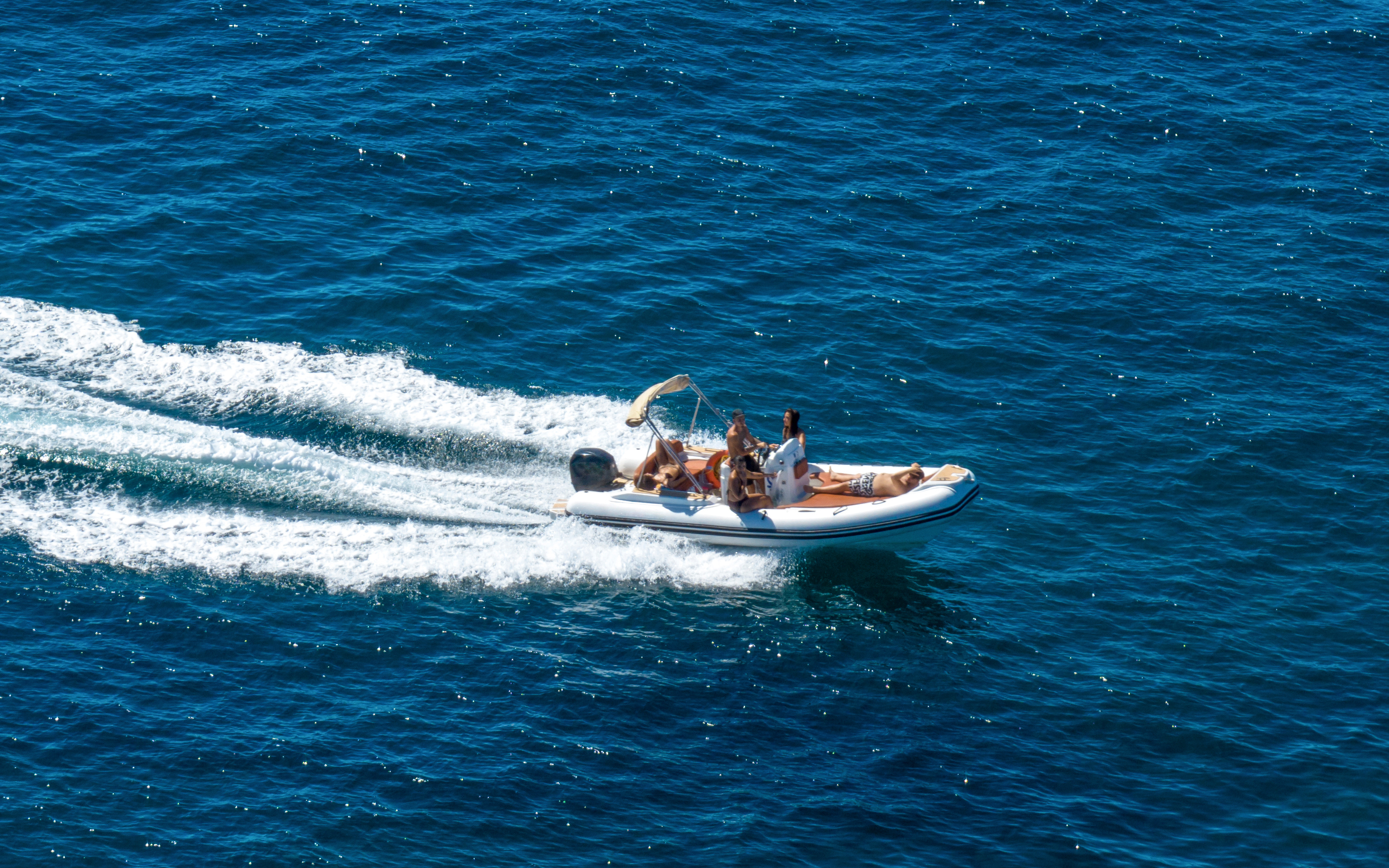 Aerial view of a dinghy with passengers cruising on open blue water.